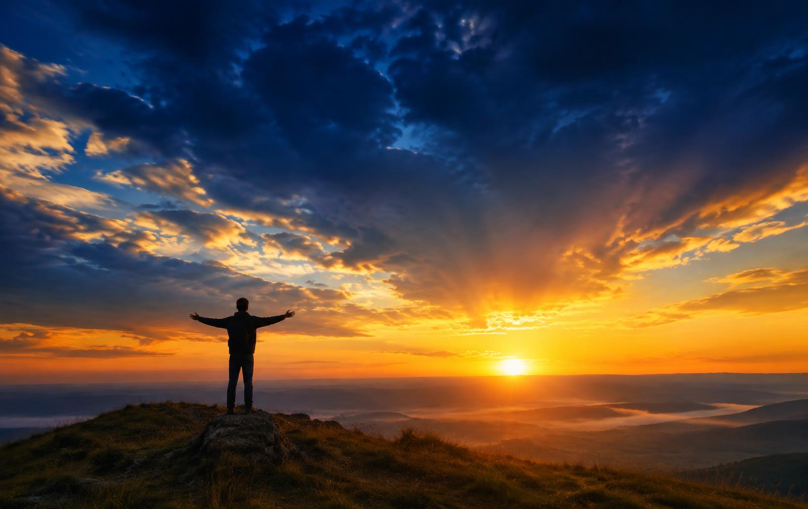 A person standing on a hill at sunrise with open arms
